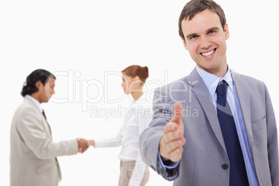 Businessman extending hand with hand shaking colleagues behind h
