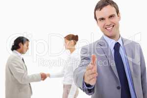 Businessman extending hand with hand shaking colleagues behind h