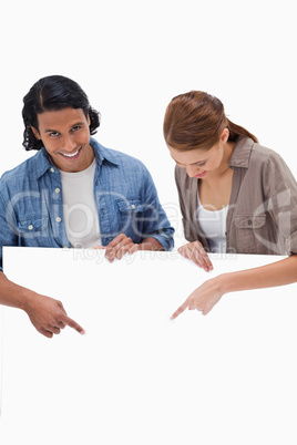 Smiling couple pointing down on blank wall