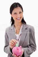 Smiling businesswoman putting money into piggy bank