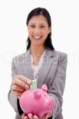 Money being put into piggy bank by smiling businesswoman
