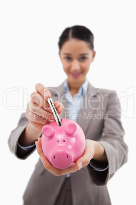 Portrait of a young businesswoman putting a bank note in a piggy