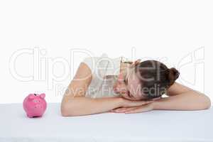 Businesswoman leaning on her desk looking at a piggy bank