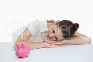 Young businesswoman leaning on her desk with a piggy bank