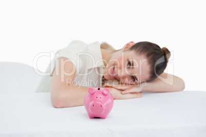 Happy businesswoman leaning on her desk with a piggy bank