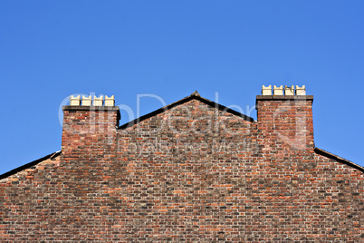 Old red brick wall with chimney pots against a clear blue sky