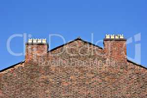 Old red brick wall with chimney pots against a clear blue sky