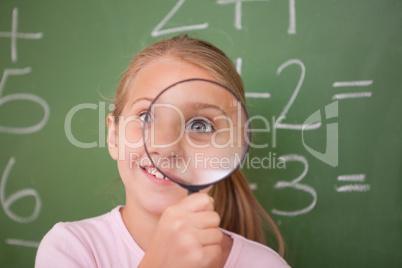 Playful schoolgirl looking through a magnifying glass