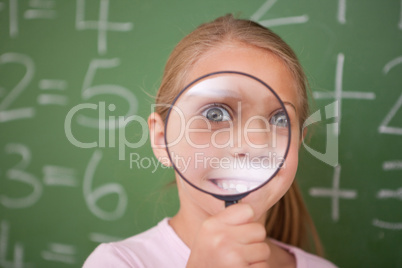 Happy schoolgirl looking through a magnifying glass