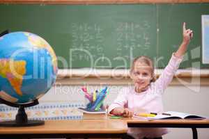 Cute schoolgirl raising her hand to answer a question