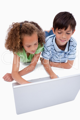 Portrait of friends using a laptop while lying on the floor