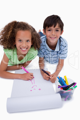 Portrait of smiling friends drawing while lying on the floor
