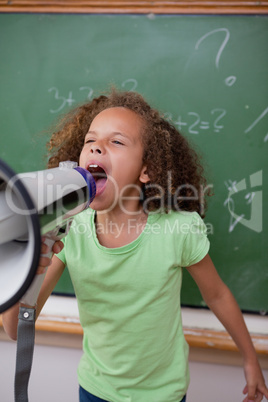 Portrait of a cute schoolgirl screaming through a megaphone