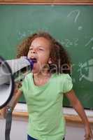 Portrait of a cute schoolgirl screaming through a megaphone