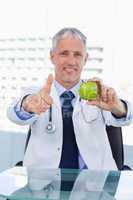 Portrait of a doctor showing an apple with the thumb up