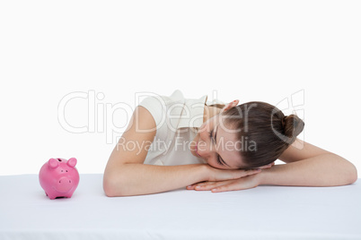 Businesswoman leaning on her desk looking at a piggy bank