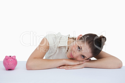 Businesswoman leaning on her desk with a piggy bank