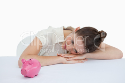 Young businesswoman leaning on her desk with a piggy bank