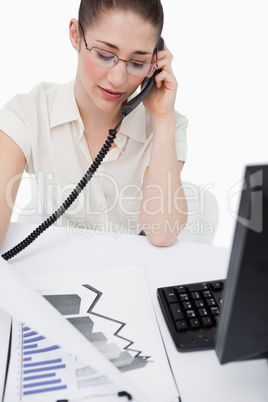 Portrait of a secretary making a phone call while looking at sta