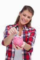 Portrait of a young woman putting a note a piggy bank