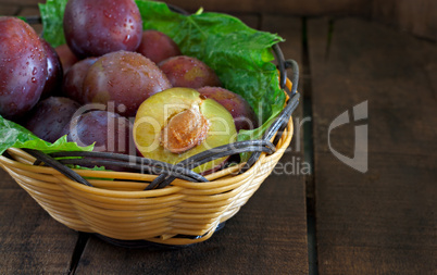 Basket of fresh plums on old wooden table