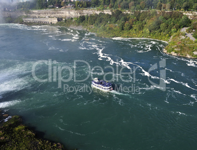 A boat in a river next to Niagara falls