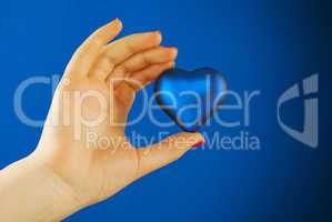 Hand holds a heart shaped gift against blue background