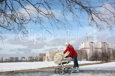 Wide shot of happy young mother in red coat with baby in buggy