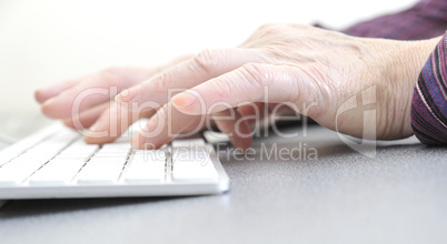 Hands of an old female typing on the keyboard, isolated on white, close-up.