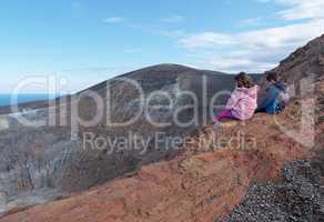 Girl and boy sitting on the rim of volcano crater of Vulcano island near Sicily, Italy