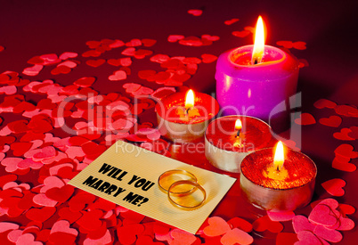 Two rings and a card with marriage proposal with four candles