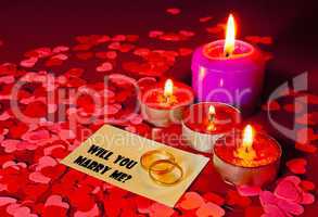 Two rings and a card with marriage proposal with four candles