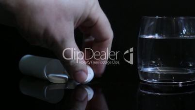 hand of man throws an aspirin into a glass of water. slider shot.