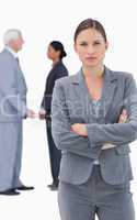 Serious businesswoman with folded arms and colleagues behind her