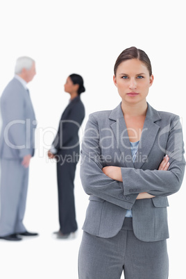 Serious businesswoman with arms folded and colleagues behind her