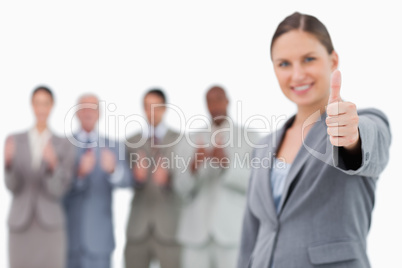 Smiling businesswoman with thumb up and colleagues behind her