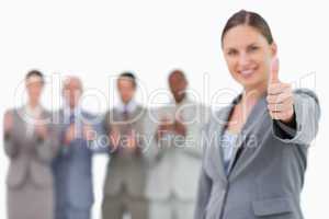 Smiling businesswoman with thumb up and colleagues behind her