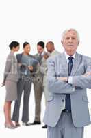 Mature businessman with arms folded and colleagues behind him