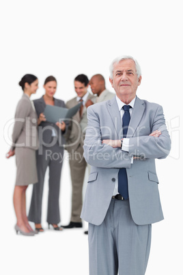 Mature businessman with arms folded and team behind him