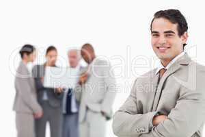 Smiling salesman with arms folded and colleagues behind him