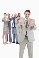 Smiling businessman with team behind him giving thumbs up