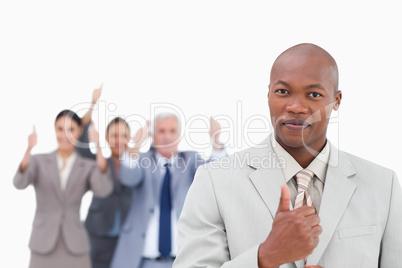 Businessman with cheering team behind him giving thumb up