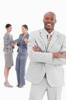 Smiling businessman with arms crossed and colleagues behind him