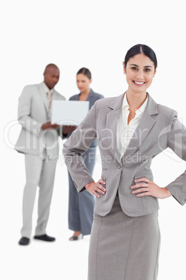 Smiling businesswoman with hands on her hip and colleagues behin
