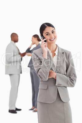 Smiling businesswoman with cellphone and colleagues behind her