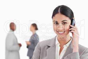 Smiling businesswoman with mobile phone and colleagues behind he