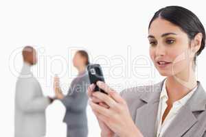 Businesswoman looking at cellphone with colleagues behind her