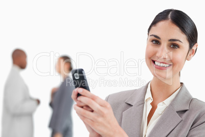 Smiling saleswoman holding cellphone with colleagues behind her