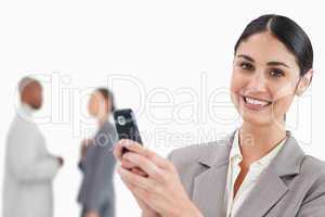 Smiling saleswoman holding cellphone with colleagues behind her