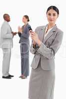 Saleswoman holding cellphone with colleagues behind her